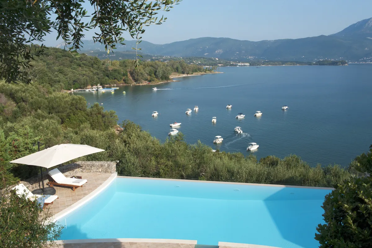 Pool terrace above a bay with moored boats at a beachfront villa in Kommeno, Corfu