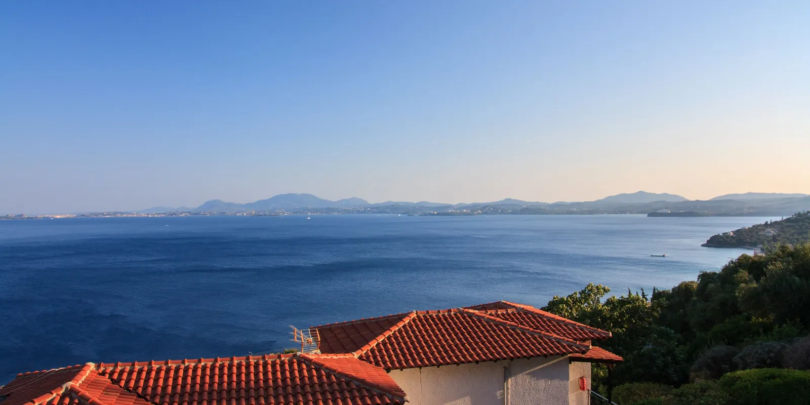 Red-roofed houses on a green Corfu hillside above the Ionian Sea at sunset