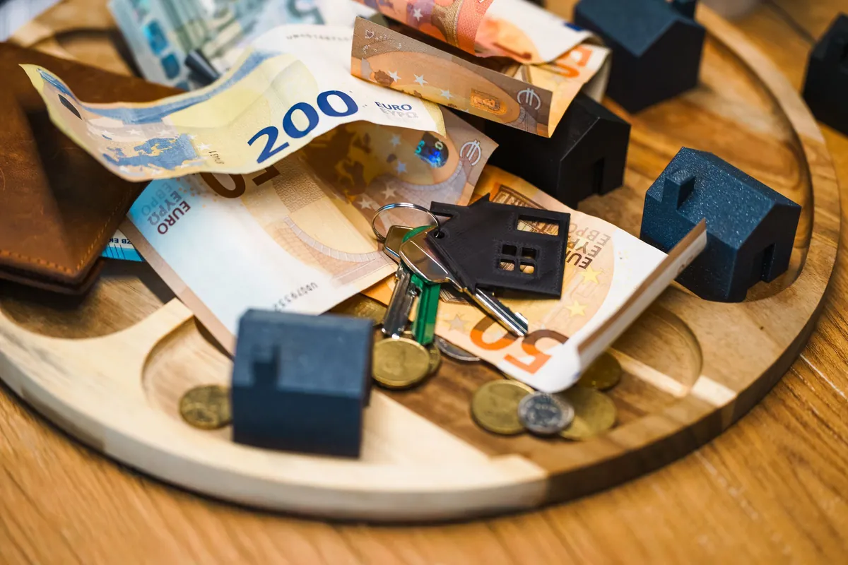 Euro banknotes, house keys and miniature houses on a table