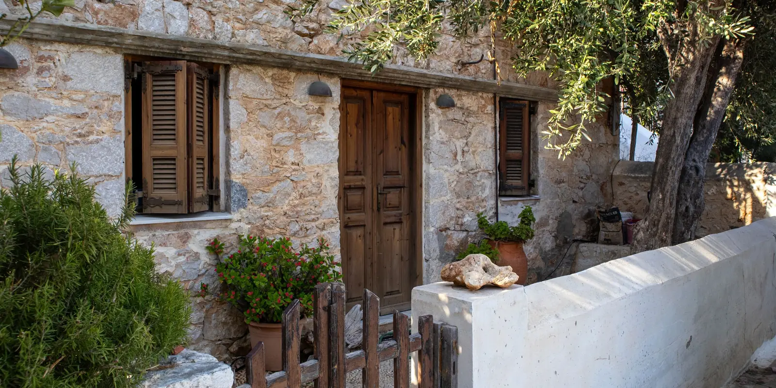 Restored stone house with wooden shutters and green surroundings on a Greek island