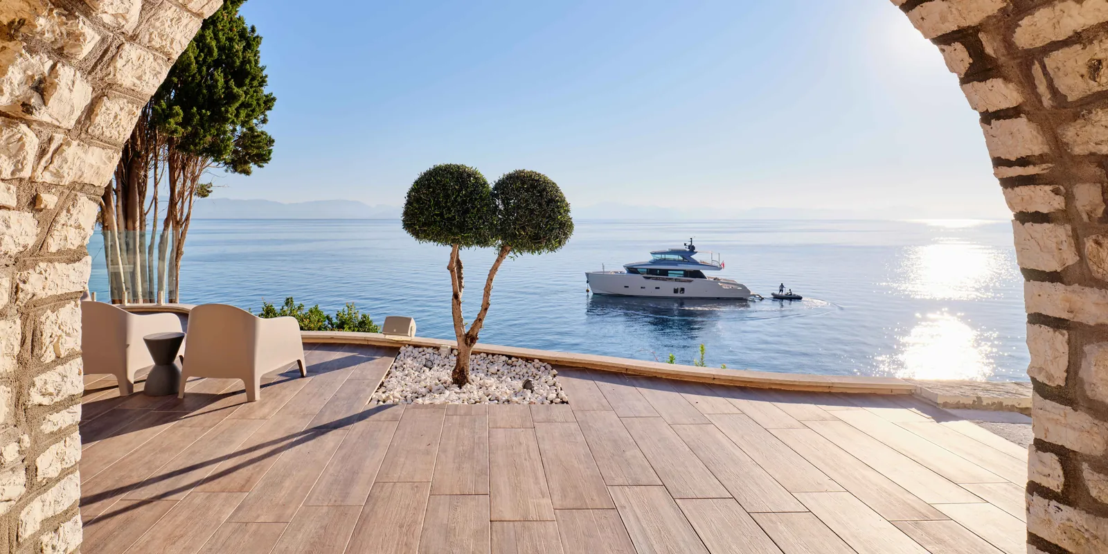 Stone arch framing the sea and a yacht from the terrace of a seafront villa estate in Benitses, Corfu