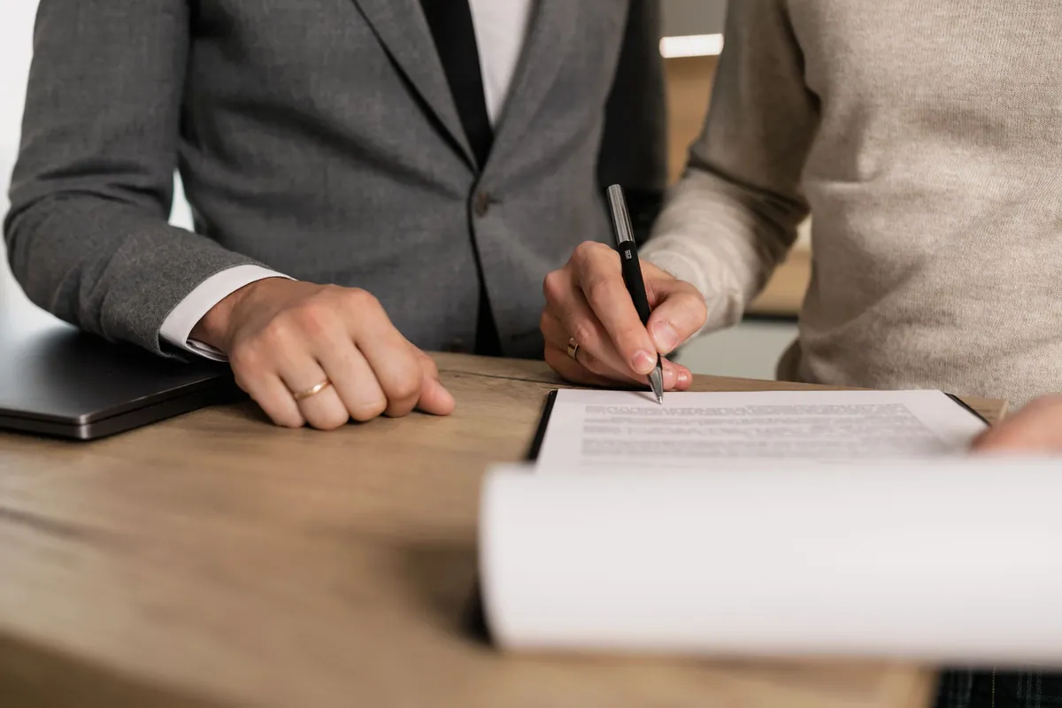 Close-up of hands signing documents at a wooden table
